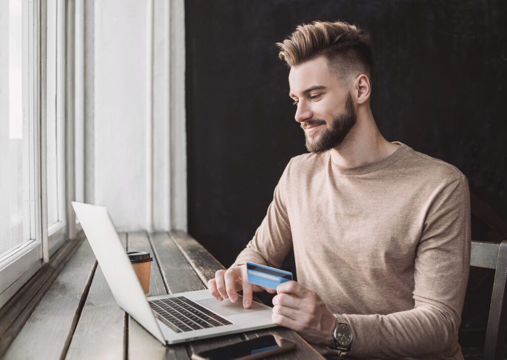 Hombre comprando en línea usando laptop y tarjeta de crédito para acumular puntos de calificación.