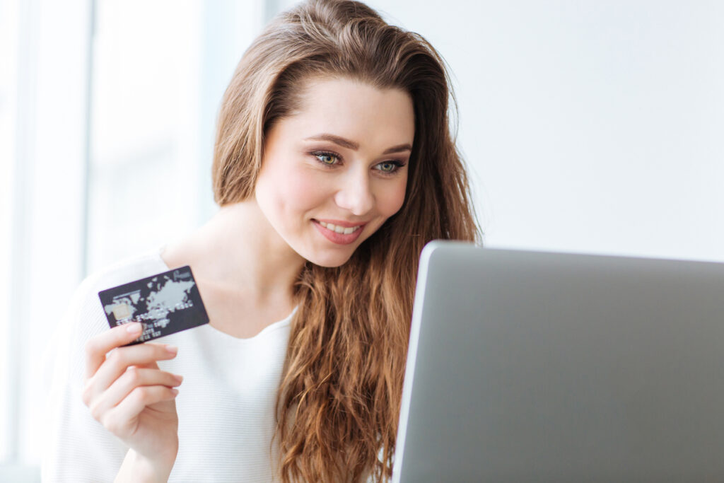 Mujer usando laptop y tarjeta de tenencia. Descubra aquí qué hacer con sus millas que caducan.