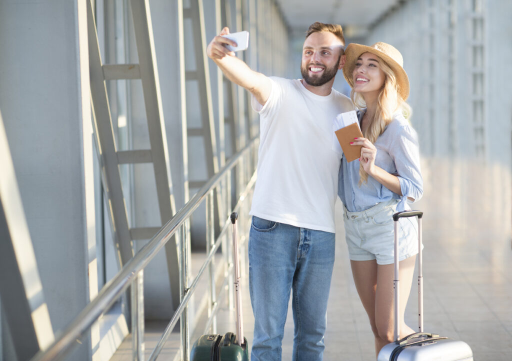 Pareja emocionada haciendo selfie en la terminal del aeropuerto. Viajar con millas es su oportunidad de visitar lugares increíbles a bajo coste.
