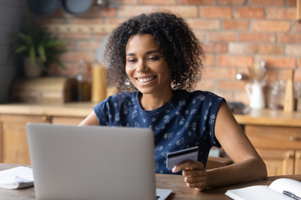 Una mujer negra está sentada sonriendo y mirando la pantalla de la computadora. MercoMillas es la mejor opcion cuándo vender millas.